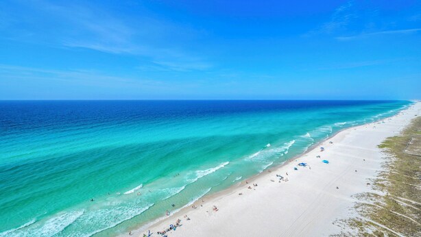 A beach with clear turquoise waters, a sandy shore, and a few umbrellas. - 5 Star Stays • Stocked Luxury Retreat • 2 Kg Suites (Panama City Beach)