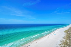 Ein Strand mit klarem türkisblauem Wasser, einem sandigen Ufer und einigen Sonnenschirmen.