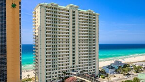 A high-rise hotel with multiple balconies, a beach view, and a pedestrian bridge. - 5 Star Stays • Stocked Luxury Retreat • 2 Kg Suites (Panama City Beach)
