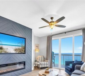 A modern living room with a fireplace, a ceiling fan, a large TV, and a view of the beach. - GulfFront Stocked Luxury Retreat • 2 King Suites (Panama City Beach)