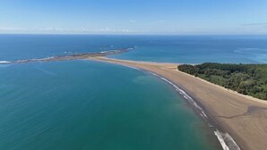 Luftaufnahme einer Küstenlandschaft mit sandigem Strand, bewaldetem Gebiet und ruhigem, blauen Wasser.