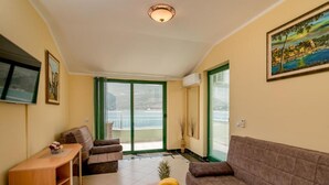 A living room with a sofa, a TV, a wooden cabinet, a fruit bowl, and a balcony with a view. - Amor Residence (Herceg Novi)