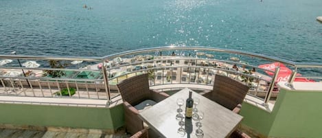 A terrace with wicker furniture, a table with wine glasses, and a view of the sea and mountains.