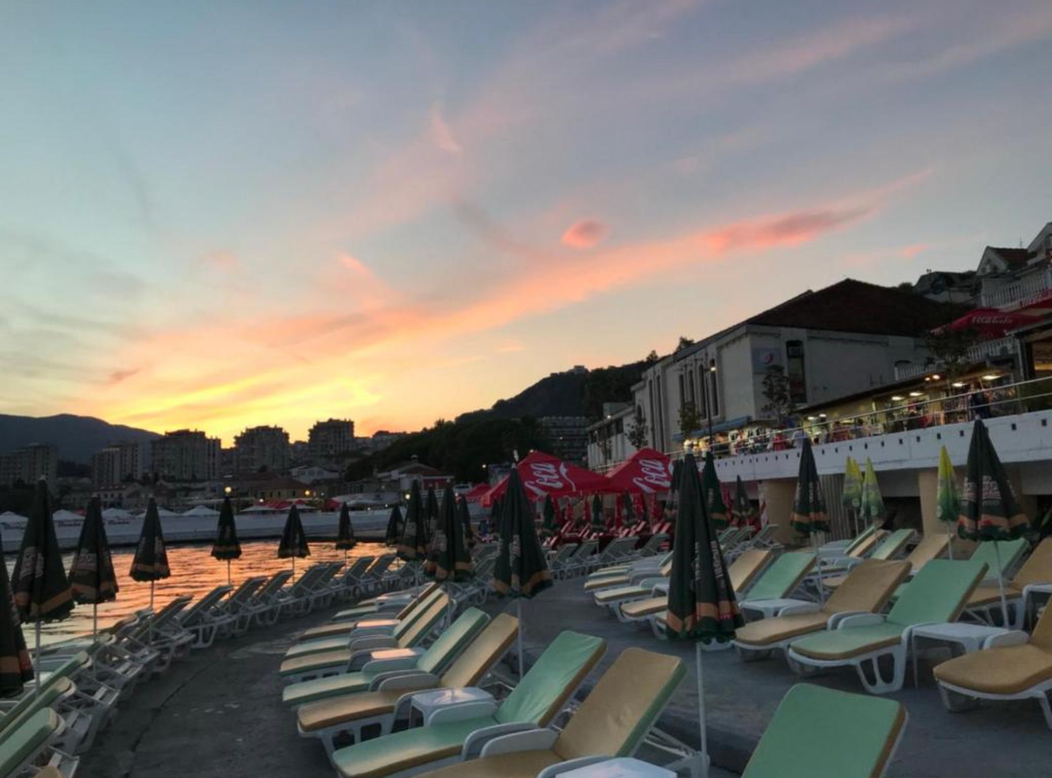 A beachside setting with rows of sun loungers and umbrellas, a building with a balcony, and a sunset in the background.