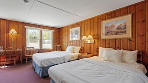 Une chambre avec deux lits, des murs en bois, un bureau, des chaises et deux lampes.