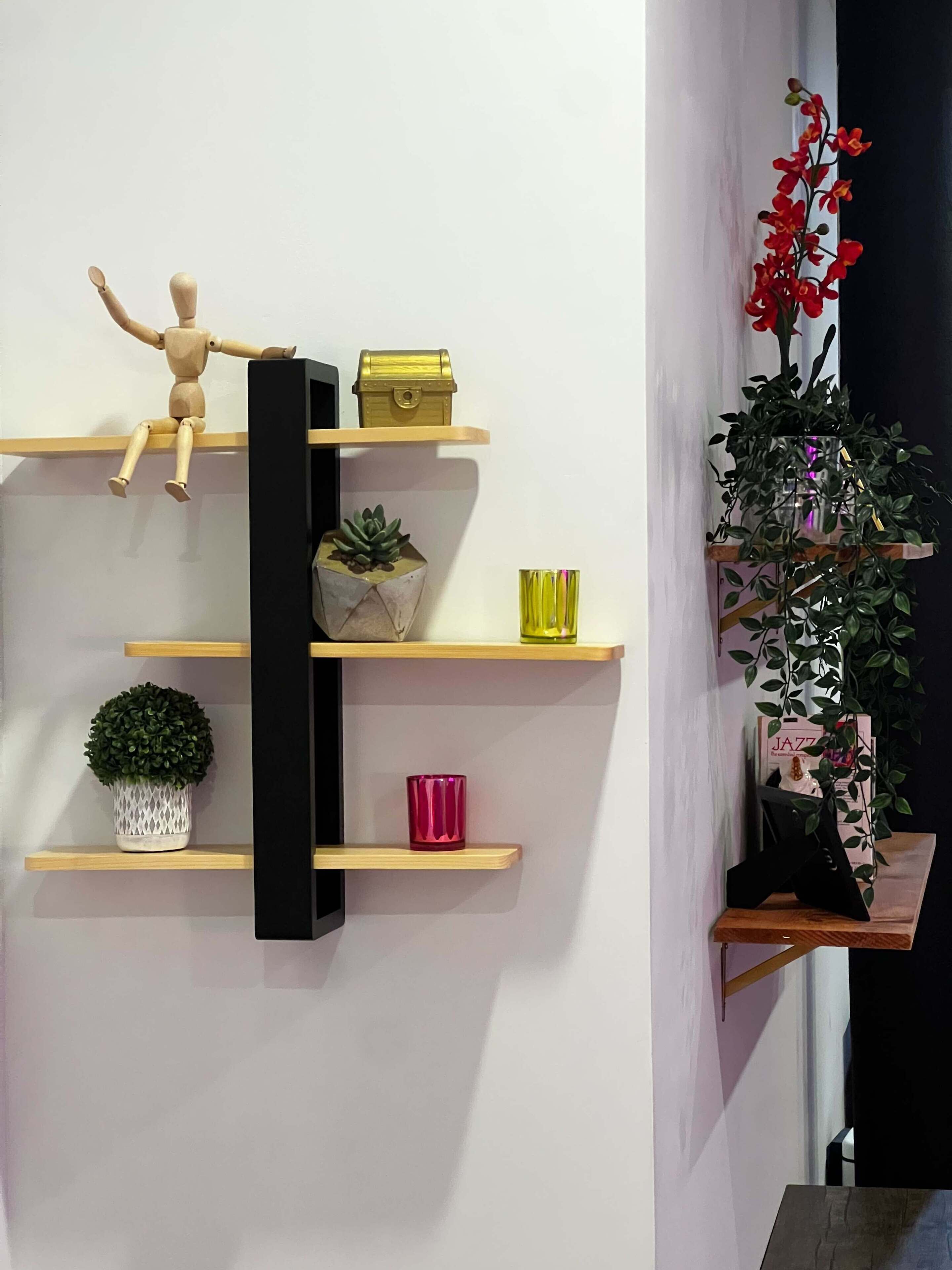 A wall with multiple shelves holding various items including a wooden figure, a small plant, a gold box, and a red vase.