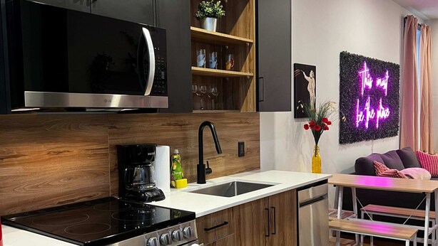 Una cocina moderna con electrodomésticos de acero inoxidable, armarios de madera, microondas integrado y un letrero de neón.