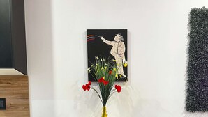 Una mesa con un jarrón amarillo de flores, un cuadro en la pared y un sofá gris.