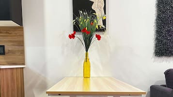 Une table sur laquelle se trouve un vase jaune rempli de fleurs, un tableau accroché au mur et un canapé gris.