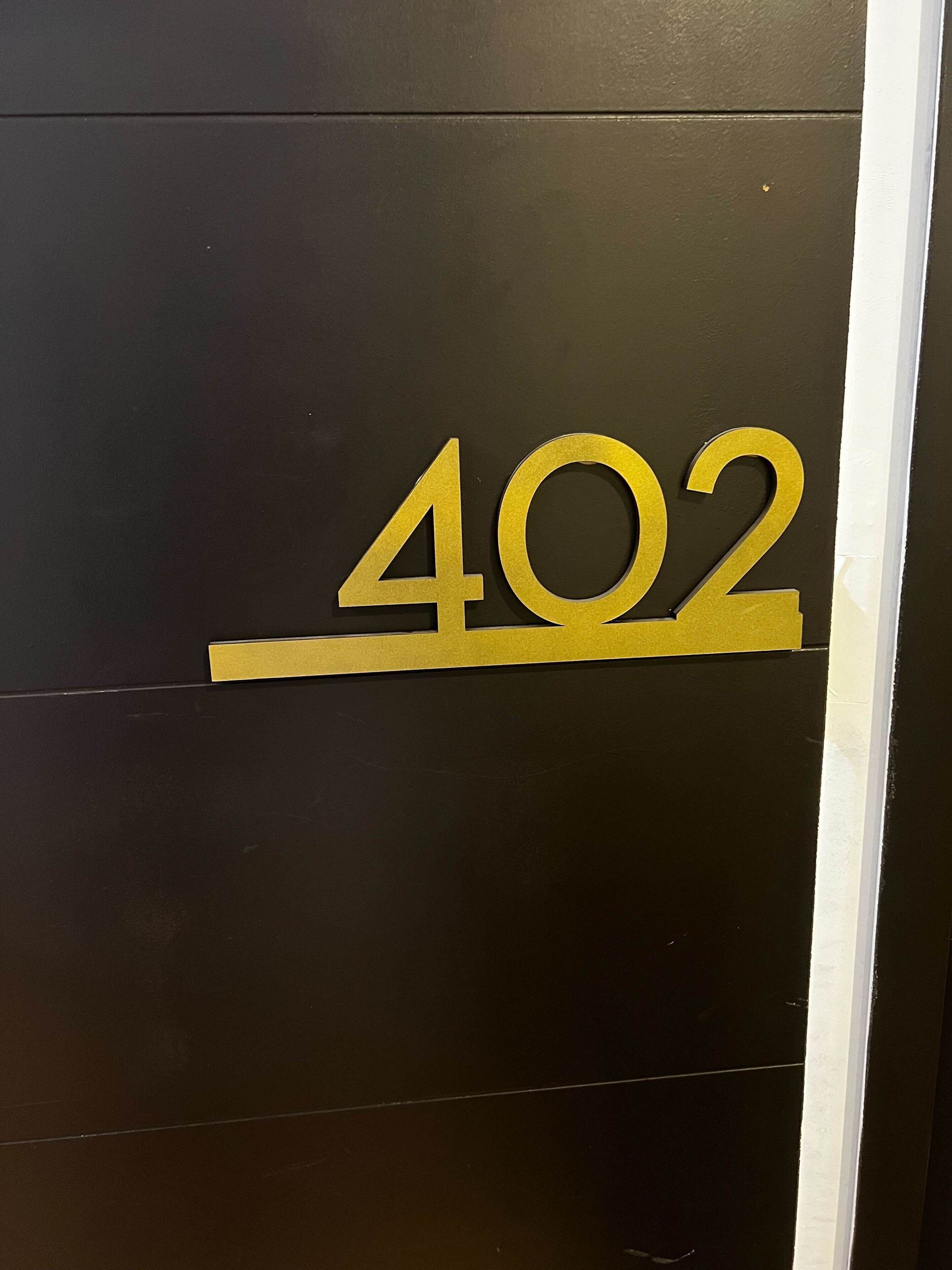 Een zwarte muur met een gouden bord met het cijfer '402'.
