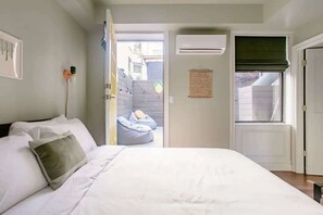 Un dormitorio con cama, ventana con persiana, equipo de aire acondicionado y vista al exterior.