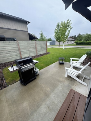 Eine Terrasse mit Grill, Gartenmöbeln und einer Betonfläche.