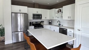 A modern kitchen with white cabinets, stainless steel appliances, a central island with bar stools, and a wooden floor. - Beautiful home in the heart of Whitefish Montana (Whitefish)