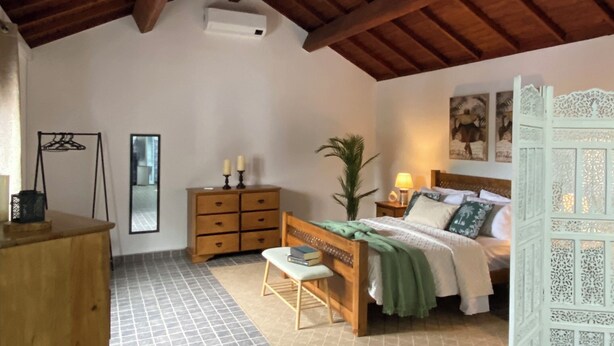 A bedroom with a sloped ceiling, a bed, a wooden dresser, a bench, and a nightstand.