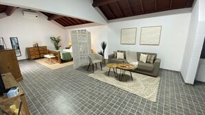 A spacious living area with a high ceiling, a sofa set, a coffee table, a side table, a chair, a bookshelf, and a decorative screen.