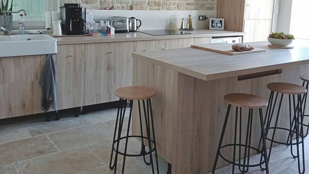 Une cuisine moderne avec un mur en pierre, des armoires en bois, un grand îlot central avec des tabourets et une machine à café.