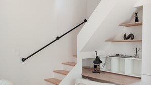 Un escalier avec des marches en bois et une rampe noire, un bureau blanc avec une lampe, une chaise en osier et un banc blanc.