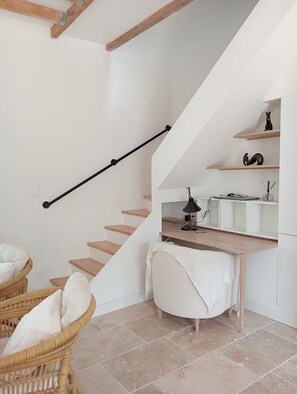 Eine Treppe mit Holzstufen und einem schwarzen Geländer, ein Schreibtisch mit Lampe, ein Korbstuhl und eine weiße Bank.