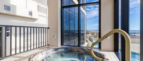 A hot tub on a balcony with a city view, large windows, and a pool.