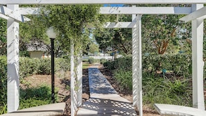 A garden pathway under a white pergola with a clear view of the surrounding greenery. - Beachwood Villas 10C - 2 Complex Pools, Tennis, Modern Coastal Charm (Santa Rosa Beach)