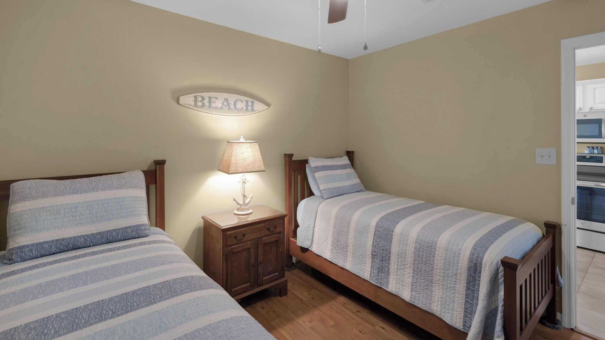 A bedroom with two single beds, a nightstand with a lamp, and a wall-mounted sign that reads "BEACH".