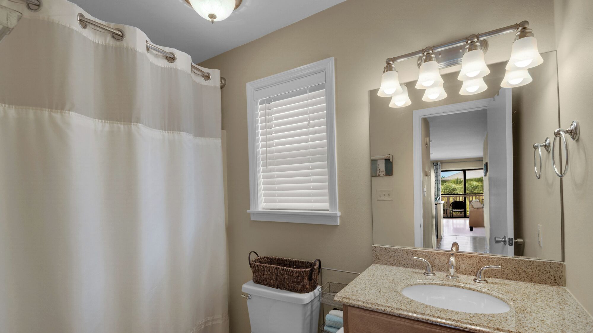 Une salle de bain avec un rideau de douche, une fenêtre avec des stores, un lavabo avec un miroir et un porte-serviettes.
