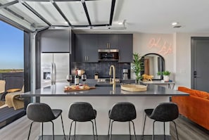 A modern kitchen with a central island, dark cabinetry, and a neon sign. - Summer rooftop deck, skyline views, garage-door kitchen near Broadway (Nashville)