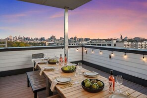 A rooftop dining area with a city view, wooden table, chairs, and string lights. - Nashville house sleeps 12, 2 decks, media room & 5 baths near Centennial Park (Nashville)