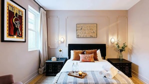 A neatly arranged bedroom with a bed, bedside tables, a chair, a framed poster, and a wall-mounted light fixture. - Nashville home with skyline decks, media room, sleeps 12 (Nashville)