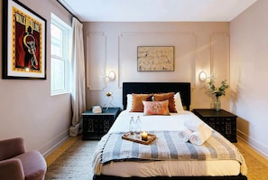 A neatly arranged bedroom with a bed, bedside tables, a chair, a framed poster, and a wall-mounted light fixture. - Rooftop retreat with game room and 4 ensuite bedrooms near Centennial Park (Nashville)