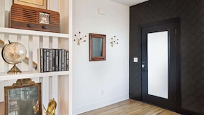 A hallway with a wooden floor, a white wall with a framed mirror, a globe, and books on a shelf. - Nashville home with skyline decks, media room, sleeps 12 (Nashville)