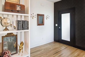Um corredor com piso de madeira, parede branca com espelho emoldurado, um globo e livros em uma estante.
