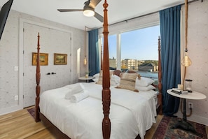 A four-poster bed with a ceiling fan, a large window with blue curtains, and a bedside table with a lamp. - Rooftop retreat with game room and 4 ensuite bedrooms near Centennial Park (Nashville)