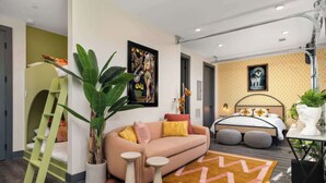 Una camera da letto moderna con un letto a castello, un divano, un tavolino e un letto con testiera decorata, più una grande pianta in vaso.