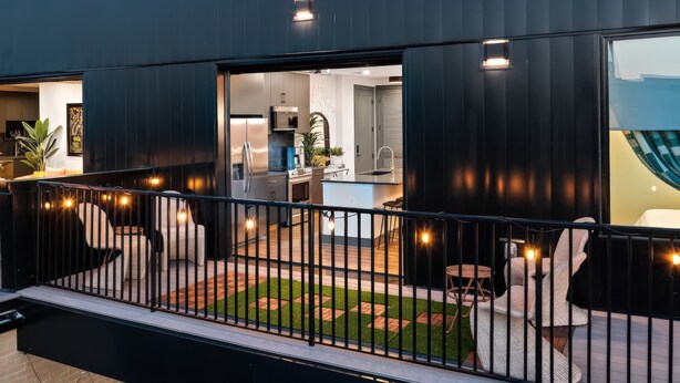 Un edificio moderno con un balcone, un'area salotto esterna e una cucina a vista.