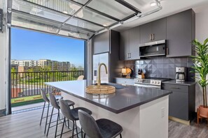 A modern kitchen with a large island, bar stools, a microwave, and a view of the outdoors. - Downtown Nashville two-home rental with rooftop deck, sleeps 8 (Nashville)