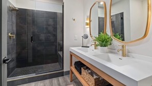 Un bagno moderno con doccia a filo pavimento, due lavabi con dettagli dorati e un grande specchio con cornice dorata.