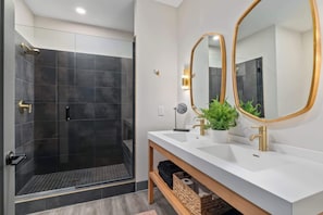 Ein modernes Badezimmer mit bodengleicher Dusche, zwei Waschbecken mit goldfarbenen Armaturen und einem großen Spiegel mit goldener Rahmung.
