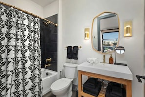 Ein modernes Badezimmer mit Toilette, Waschbecken und Dusche. Über dem Waschbecken hängt ein Spiegel und es gibt einen Blick auf Gebäude im Freien.