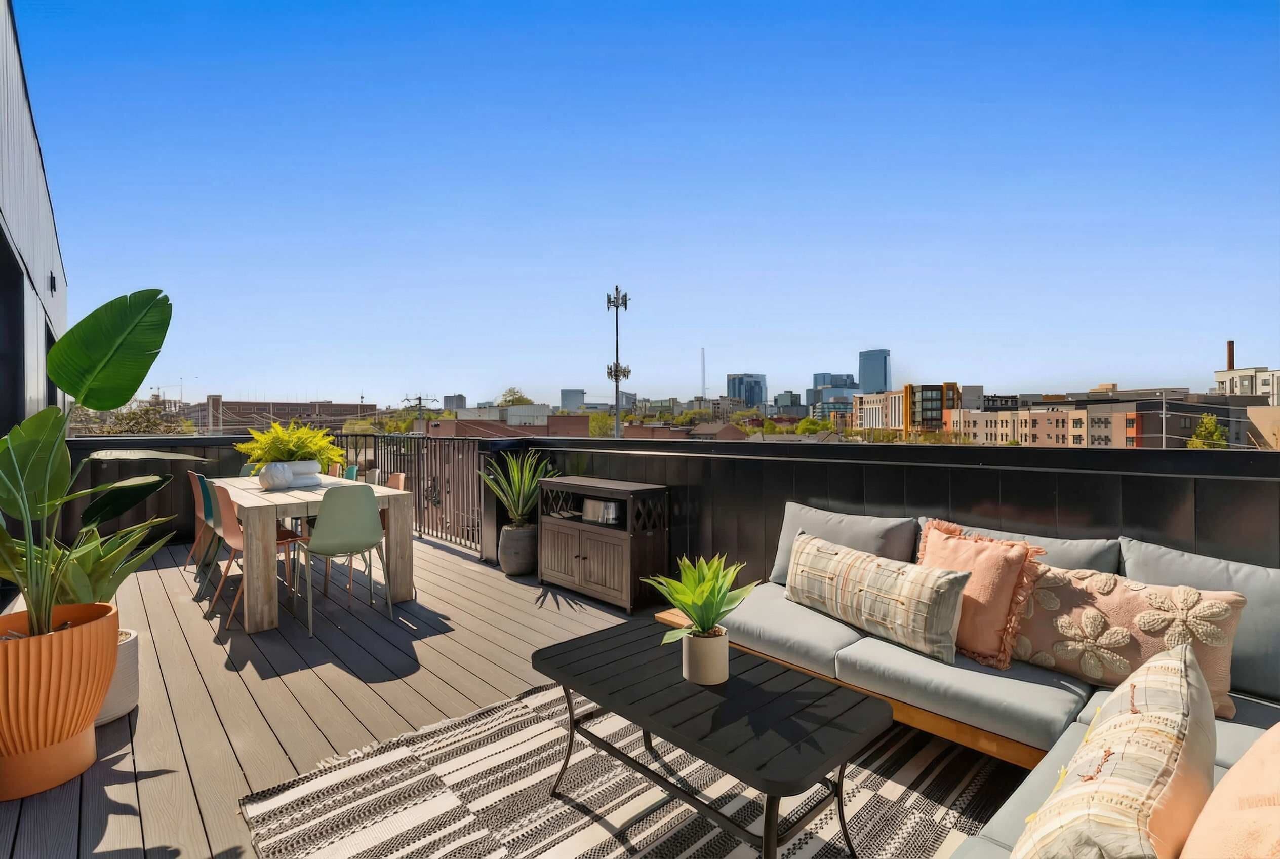A rooftop patio with a wooden table, chairs, a sofa, and potted plants.