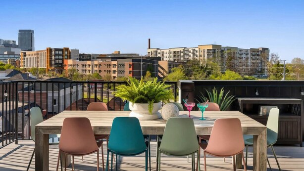 Eine Dachterrasse mit Holztisch und -stühlen, Blumentöpfen und Cocktailgläsern.