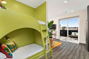 Ein Stockbett mit einer Leiter, ein kleiner Tisch mit Büchern und ein großes Fenster mit Blick auf die Stadt.