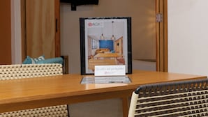 Uma mesa de madeira com um quadro emoldurado de um quarto, uma placa com uma pergunta e cadeiras de vime.
