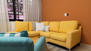 Uma sala de estar com um sofá amarelo, uma poltrona azul e um tapete listrado.