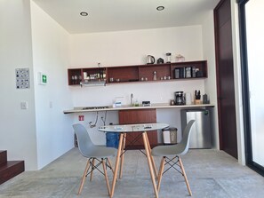 Cozinha moderna com fogão a gás, cafeteira e geladeira. Há duas cadeiras e uma mesa redonda pequena.
