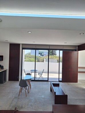 A modern room with a glass door leading to an outdoor area, a small table with chairs, and a bench. - POSTAL 3 · Apt with garage and terrace w/views close downtown (Oaxaca)