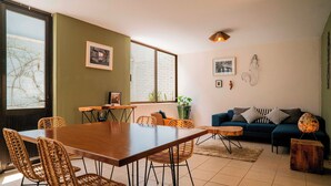 Un coin repas avec une table en bois et des chaises en osier, un canapé avec des coussins et une plante en pot.