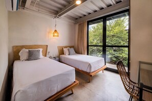 Ein Zimmer mit zwei Betten, einem Holzstuhl, einem Schreibtisch und einem großen Fenster mit Blick auf Grünflächen.