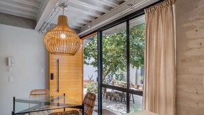 Ein modernes Interieur mit Glastisch, Korbstühlen, einer Holzwand und einem großen Fenster mit Vorhängen.