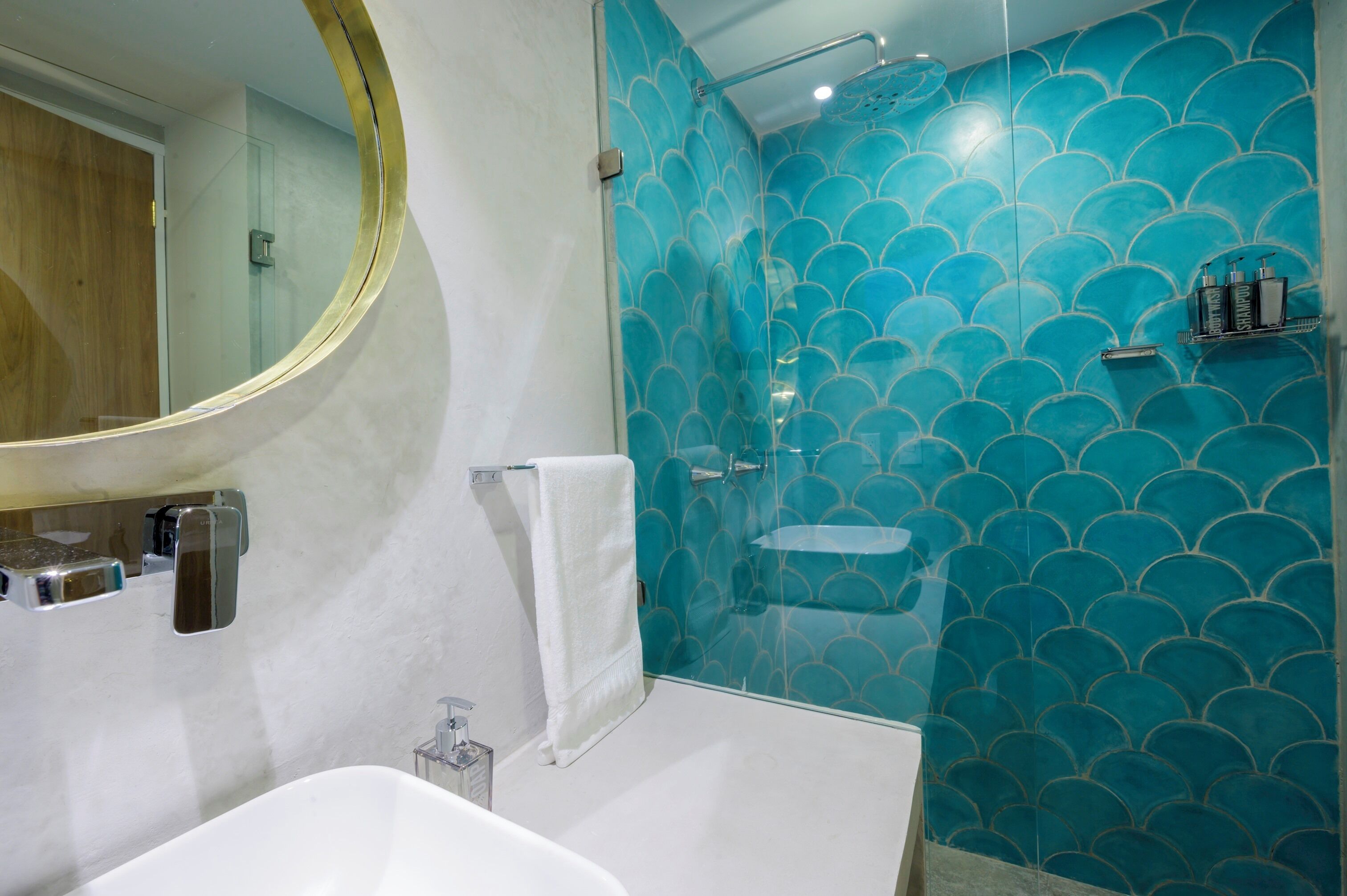 Une salle de bain avec un lavabo blanc, un miroir, une douche en verre et un mur orné d’un motif bleu en forme de coquillages.